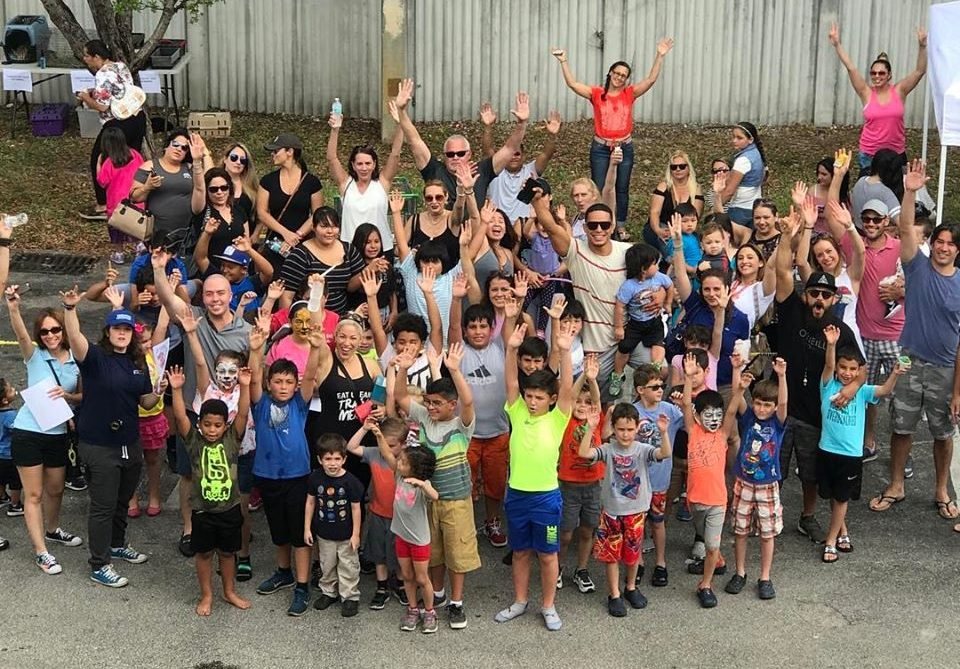 A large group of kids and adults outdoors, waving at the camera