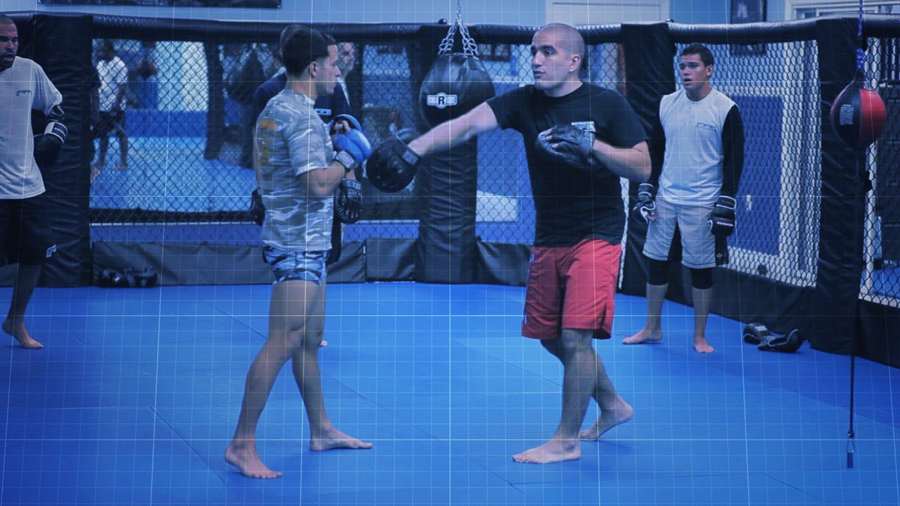 Two students doing pad work inside the cage while others watch